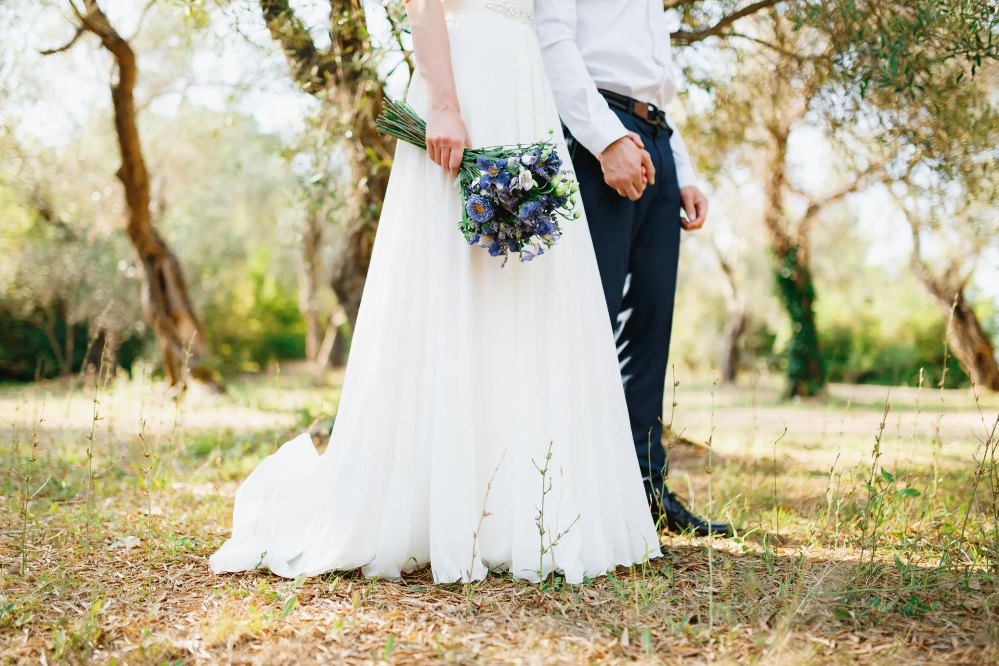 Couple standing among olive trees, the bride holding a bouquet